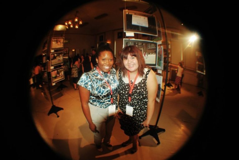 Two people standing behind a theatre stage smiling, Jessie Goyette is on the right