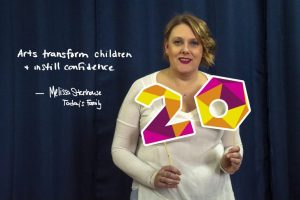 Today's Family Melissa standing infron of curtain holding colourful twenty sign with a smile. Text beside Melissa reads "Arts transform children and instill confidence" - Melissa Stenhouse