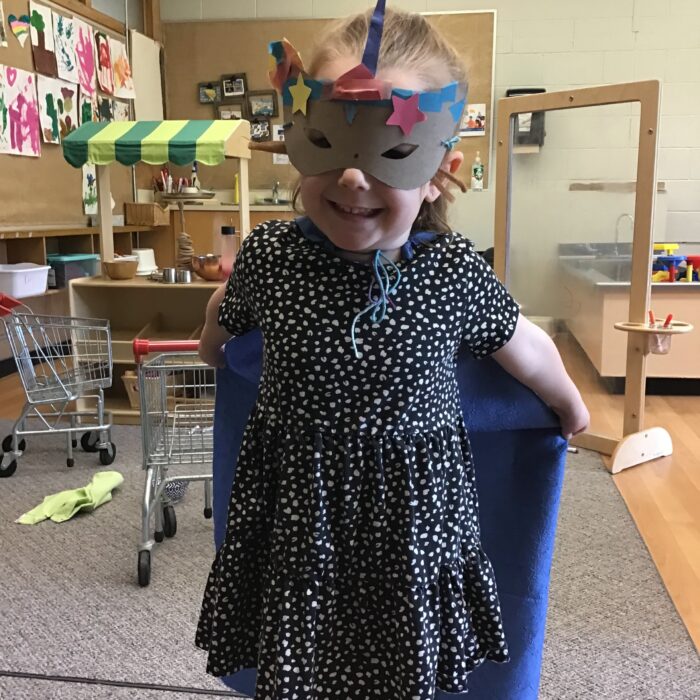Little girl smiling. She is wearing a cape and mask
