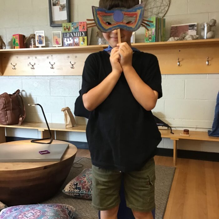 Child holding guardian mask and wearing a cape